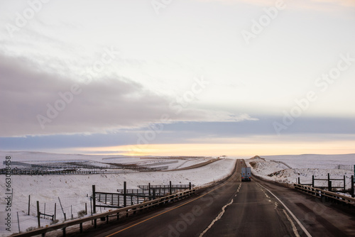 Beautiful winter landscape with a highway between blue snowy mountains  fluffy clouds on a sunset orange sky. Winter snow background. Elk Mountain  Wyoming  USA. Picturesque winter sky