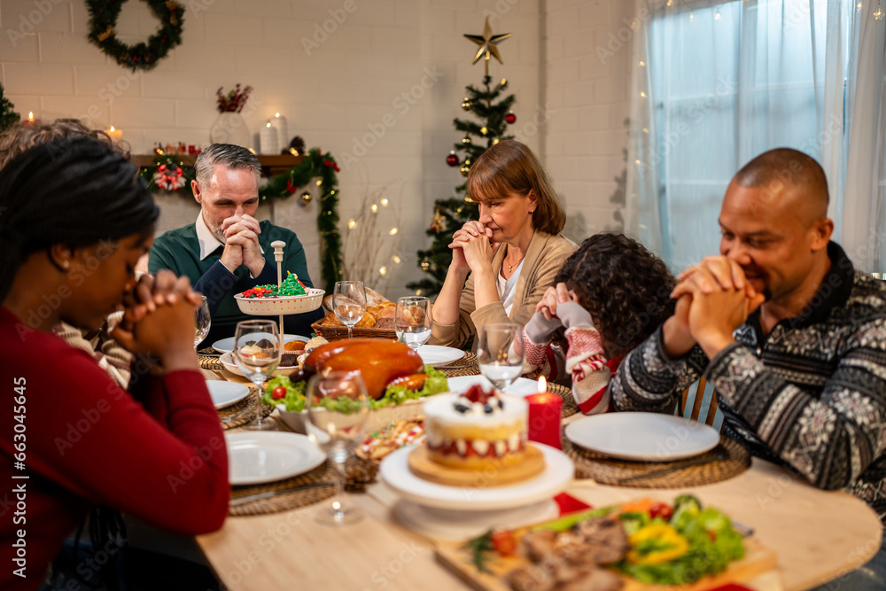 Multi-ethnic big family saying a prayer before having Christmas dinner. 