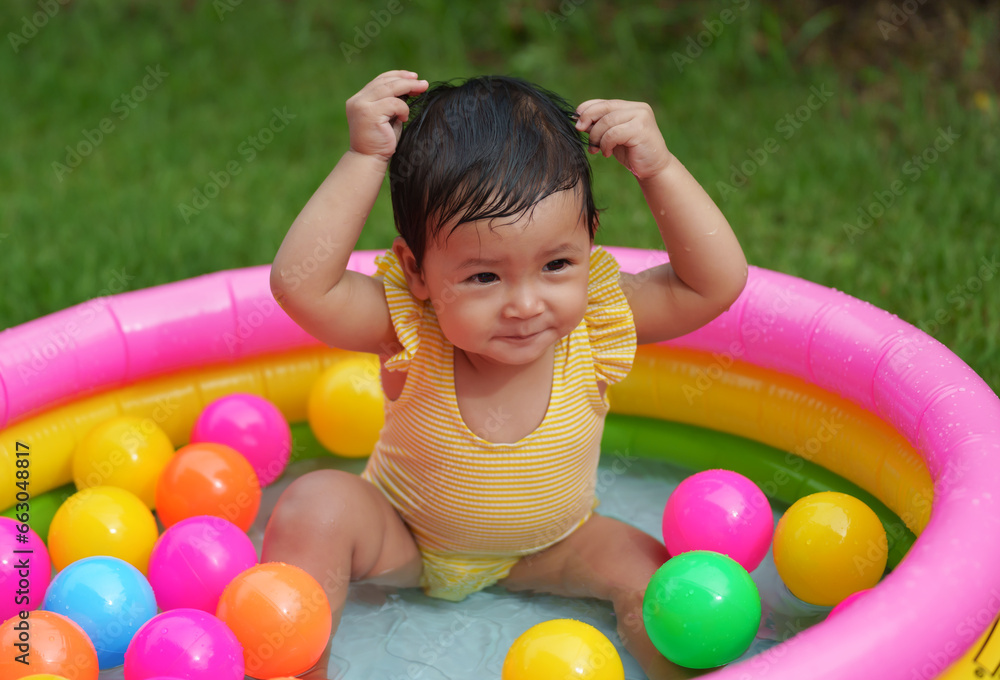 Obraz premium happy infant baby girl playing water with colorful plastic balls in inflatable pool