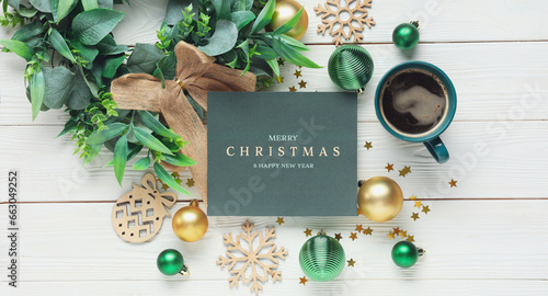 Beautiful Christmas composition with greeting card, decorations and cup of coffee on white wooden background, top view