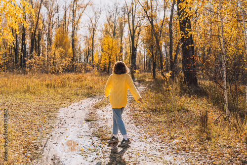 A girl in a yellow knitted sweater walks through the autumn forest.