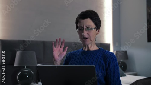 Senior woman make video call waves hand sitting on the couch.Middle age lady using laptop for communication online, webcam zoom conference at home.