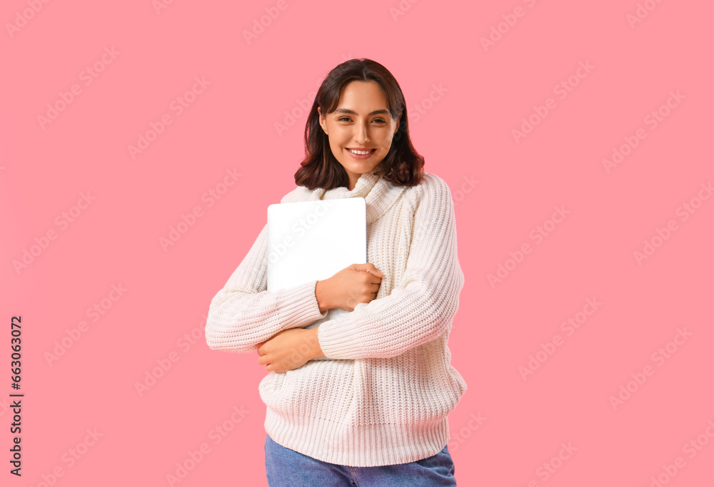Young woman in warm sweater with laptop on pink background Young woman in warm sweater with laptop on pink background