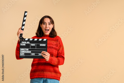Surprised young woman in red sweater with movie clapper on beige background © Pixel-Shot