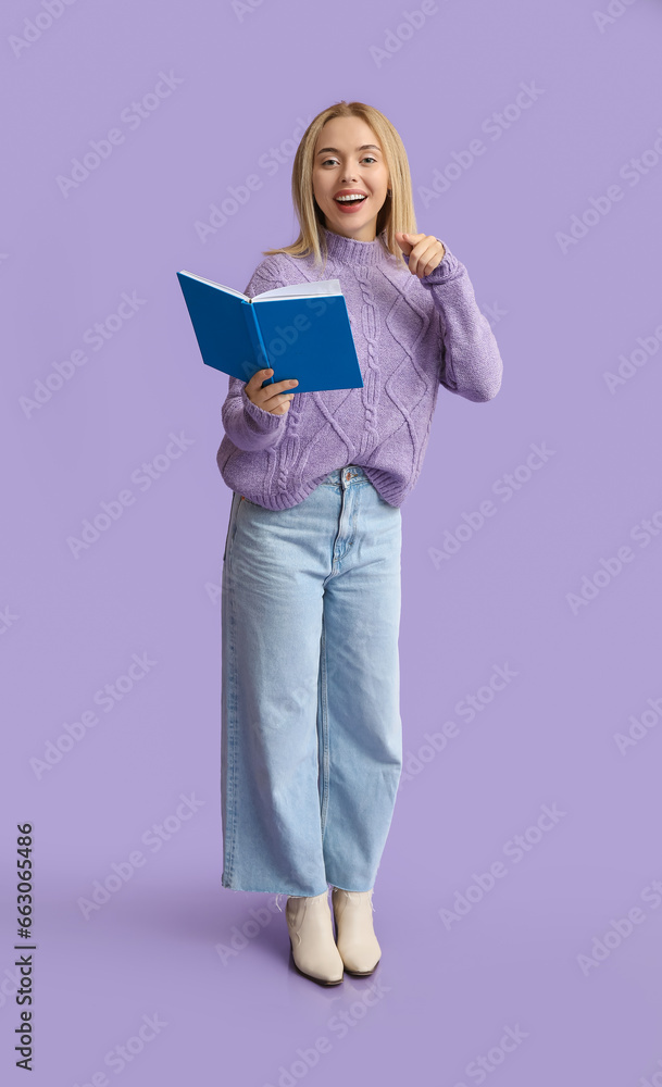 Beautiful young happy woman with book pointing at viewer on lilac background Beautiful young happy woman with book pointing at viewer on lilac background