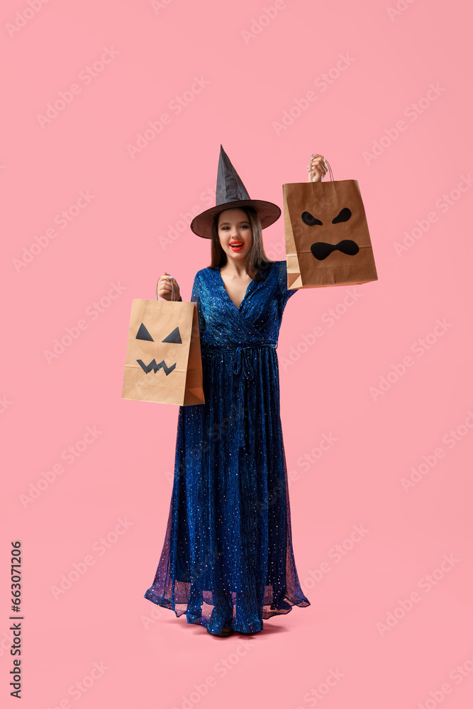 Young woman dressed for Halloween as witch with gift bags on pink background
