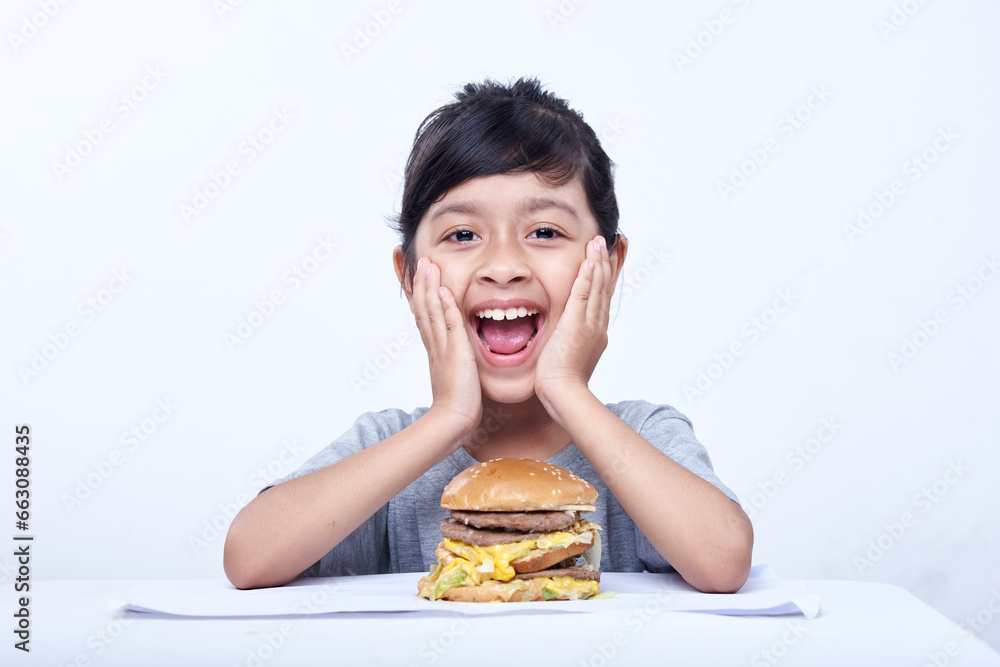 Smiling Little girl with a big cheeseburger with tomato, lettuce, arugula, beef and sauce