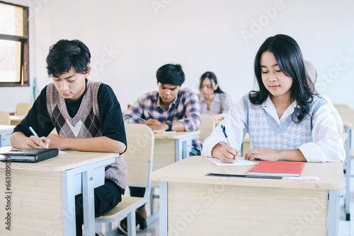Group of high school students sitting in classroom and writing in notebooks.