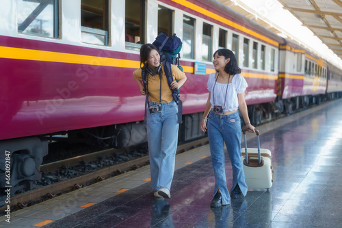 Two young Asian women traveler with a backpack on the railway, Backpack at the train station with a traveler, Travel concept. Women traveler tourists walking at a train station.