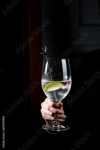 transparent cocktail with lime in a wine glass on a dark background side view