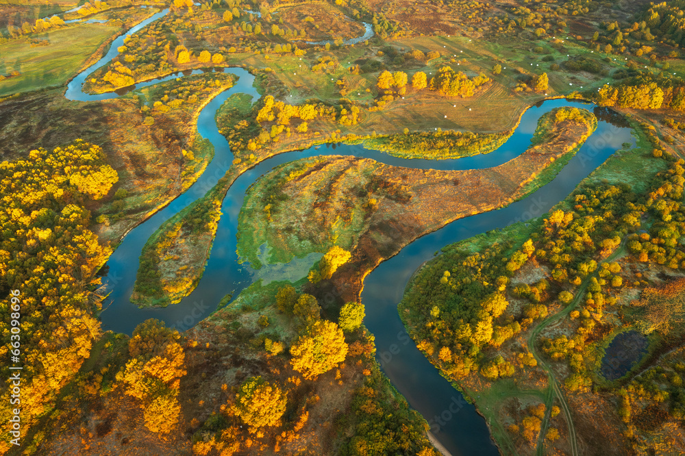 Aerial view of landscape of a winding river in autumn morning. The sky is reflected from the surface of the river. Sunbeams illuminate the trees and grass and change their color to light green.