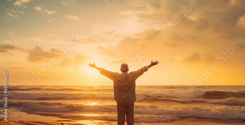 silhouette of an old man with stretched arms greeting the sun on a beach