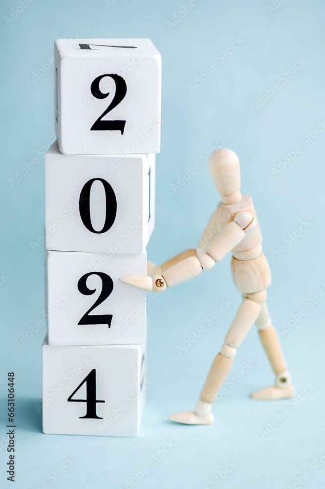Wooden man holding wooden cubes with numbers 2024 on a blue background.New Year concept. Vertical photo