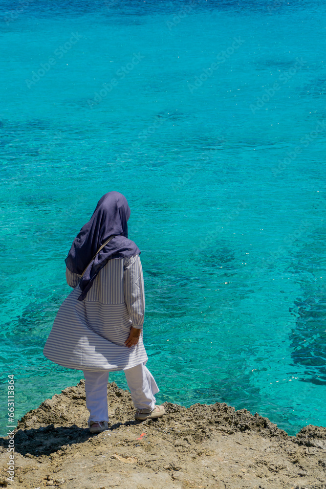 Traveling concept. Young asian hijab girl standing on the rock at Ujung Karang beach in Sabang island, Indonesia.