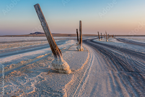 Road on salt lake Baskunchak (Russia), marked with logs at sunset or sunrise. The base of the logs was covered with a thick layer of salt. Landscape in the morning or evening against the Big Bogdo.
