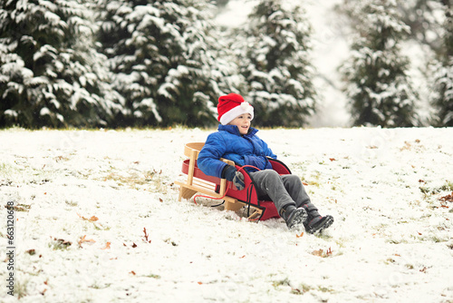 Boy wearing Santa hat sledding down a hill in winter