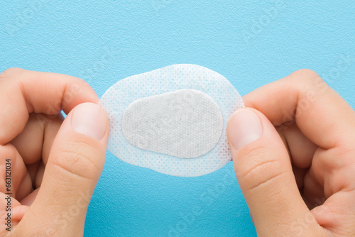 Cuadro en lienzo Young adult woman hand fingers holding and showing white new sticking plaster for eye covering on light blue table background
