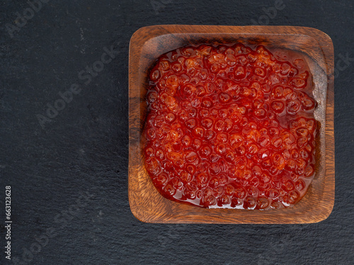 Wooden cup with red caviar on a black slate stone. Red caviar close-up.