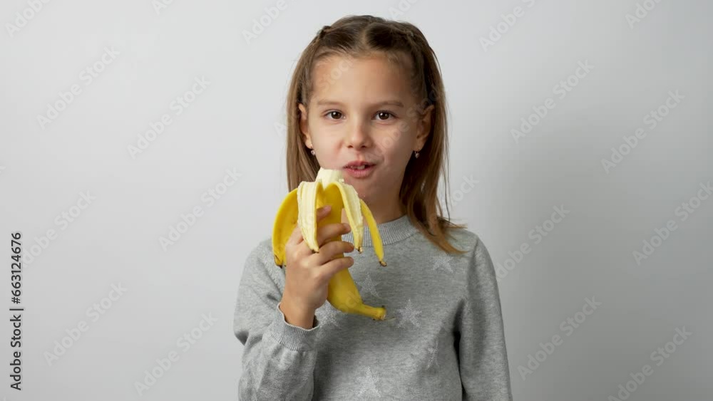 Child girl peeling and eating banana, white background Child girl peeling and eating banana, white background