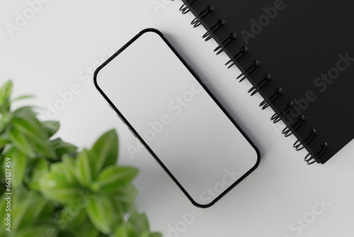Top view of smartphone with empty screen, notebook and indoor plant on wooden table