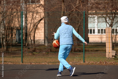 A child of 10 years old plays basketball on an open sports ground. Girl playing with a ball outdoors on an autumn day.