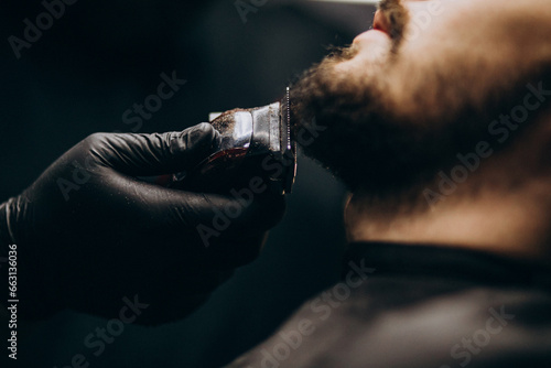 Fototapete Handsome man cutting beard at a barber shop salon
