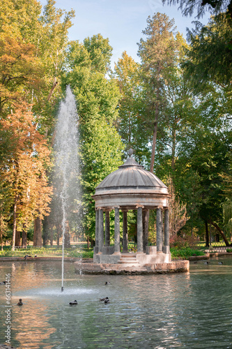2023-07-20, Aranjuez, Spain: A fountain in a pond surrounded by ducks and trees in the Spanish gardens of Aranjuez. A gazebo with a stone dome sits in the center of the pond