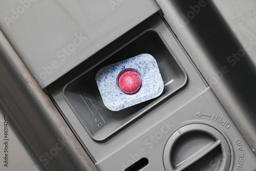 Dishwasher detergent dispenser. Closeup red ball washing pod. Cleaning capsules inside dispenser. Washing dishes background. Dishwasher part closeup. Pods cup part. photo