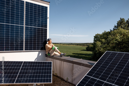Man sitting on a rooftop of his house with a solar power station installed on it. Renewable green energy and sustainability concept