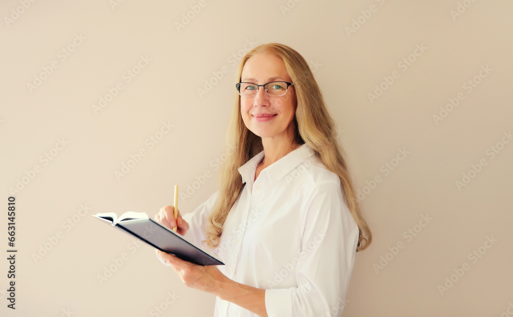 Portrait of happy caucasian middle-aged woman in eyeglasses writing down memories in notebook diary on studio background Portrait of happy caucasian middle-aged woman in eyeglasses writing down memories in notebook diary on studio background