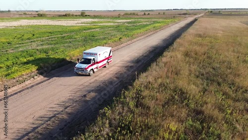 Drone footage of an ambulance car driving on an unpaved rural road in the fields photo