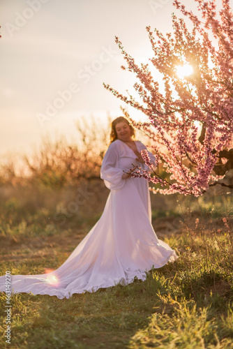 Woman blooming peach orchard. Against the backdrop of a picturesque peach orchard, a woman in a long white dress enjoys a peaceful walk in the park, surrounded by the beauty of nature.