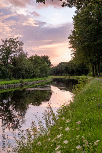 A captivating scene of a dramatic purple-pink sky with beautifully articulated clouds, bathed in the setting sun's glow, mirrored in the tranquil waters of a serene river or canal. Dramatic Purple