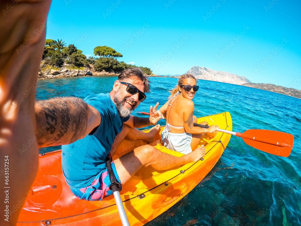 Happy couple of tourist taking selfie inside a kayak canoe in summer holiday travel vacation smiling and having fun at the camera. Cheerful man and woman on a boat. Blue clean beautiful sea ocean - obrazy, fototapety, plakaty 