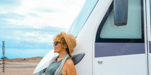 One solo traveler woman enjoy arrival destination standing outside a modern big rv vehicle camper van motorhome admiring landscape desert nature around. Blue sky in background. Lifestyle female people
