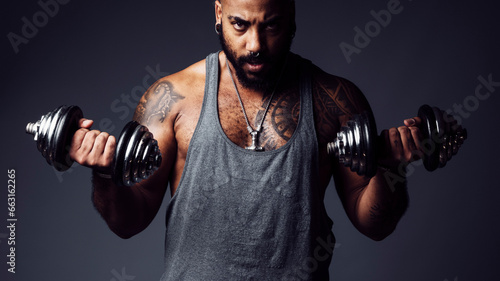 Black man with defiant attitude looks at camera holding two dumbbells in a studio shot photo