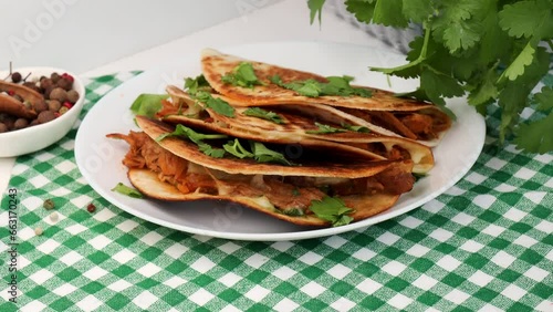 Quesabirria tacos is a Mexican dish that consists of spicy, shredded beef and melted cheese enclosed in tortillas. The girl sets a plate of tacos on the table, accompanied by a green napkin photo