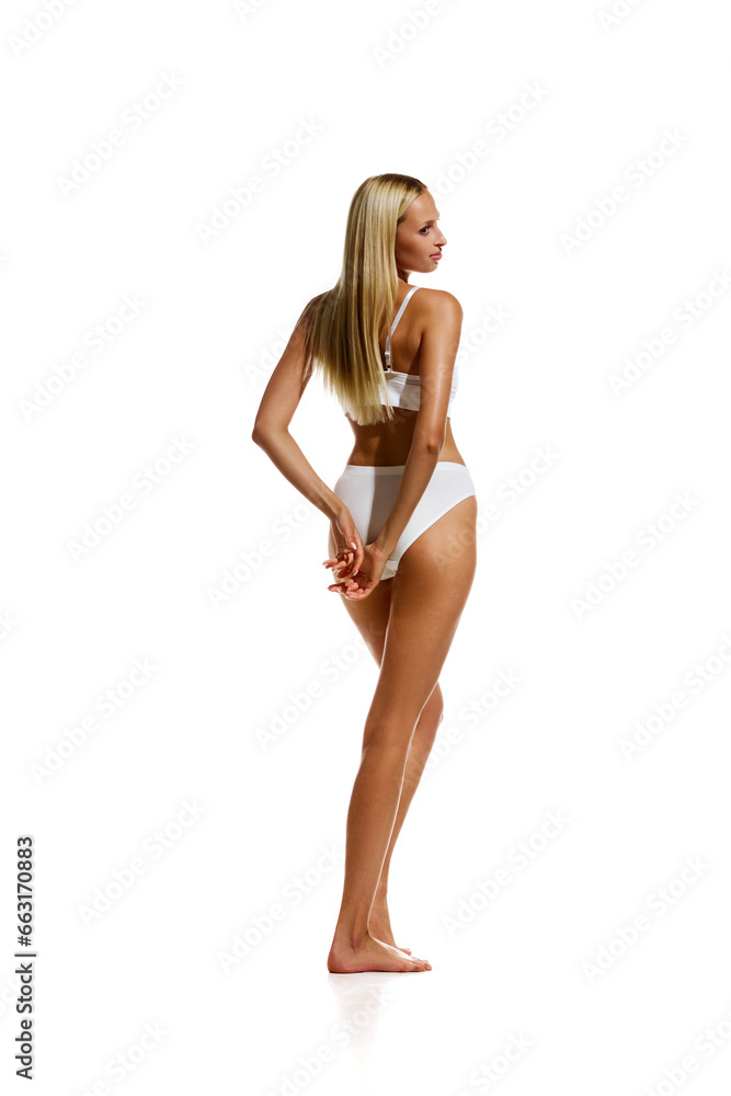 Full-length back view image of slim young girl with smooth tanned body standing in underwear against white studio background. Concept of natural beauty, body and skin care, health, sport, wellness.
