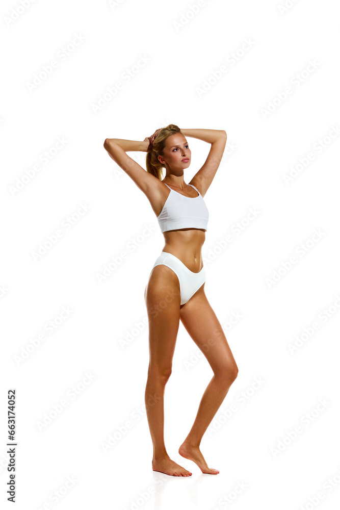 Full-length image of attractive young girl with beautiful, fit, slim body standing in underwear against white studio background. Concept of natural beauty, body and skin care, health, sport, wellness. Full-length image of attractive young girl with beautiful, fit, slim body standing in underwear against white studio background. Concept of natural beauty, body and skin care, health, sport, wellness.