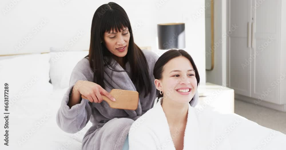 Happy biracial mother in bathrobe brushing hair of smiling adult daughter in sunny room, slow motion Happy biracial mother in bathrobe brushing hair of smiling adult daughter in sunny room, slow motion