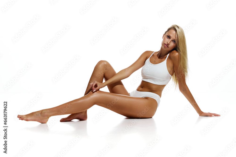 Beautiful, young, blonder girl with tanned, fit, slim body sitting in cotton underwear over white studio background. Concept of natural beauty, body and skin care, sport, wellness. Copy space for ad Beautiful, young, blonder girl with tanned, fit, slim body sitting in cotton underwear over white studio background. Concept of natural beauty, body and skin care, sport, wellness. Copy space for ad