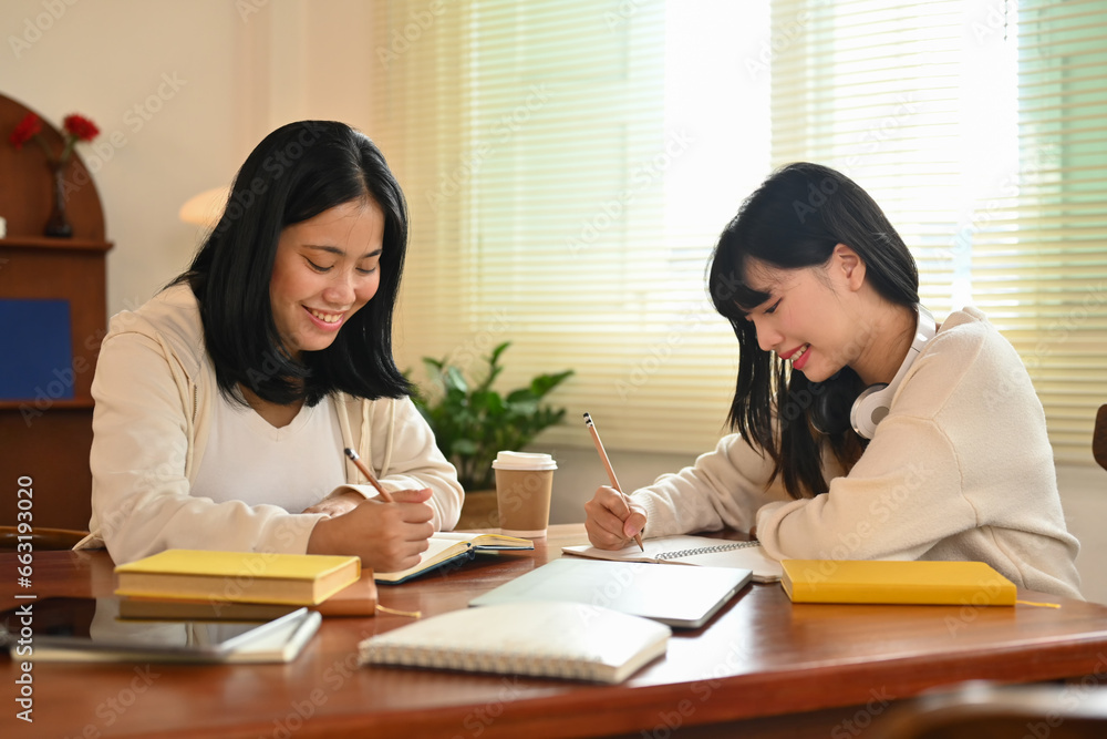 Two smiling university student discussing their home assignment in library. Education and lifestyle concept Two smiling university student discussing their home assignment in library. Education and lifestyle concept