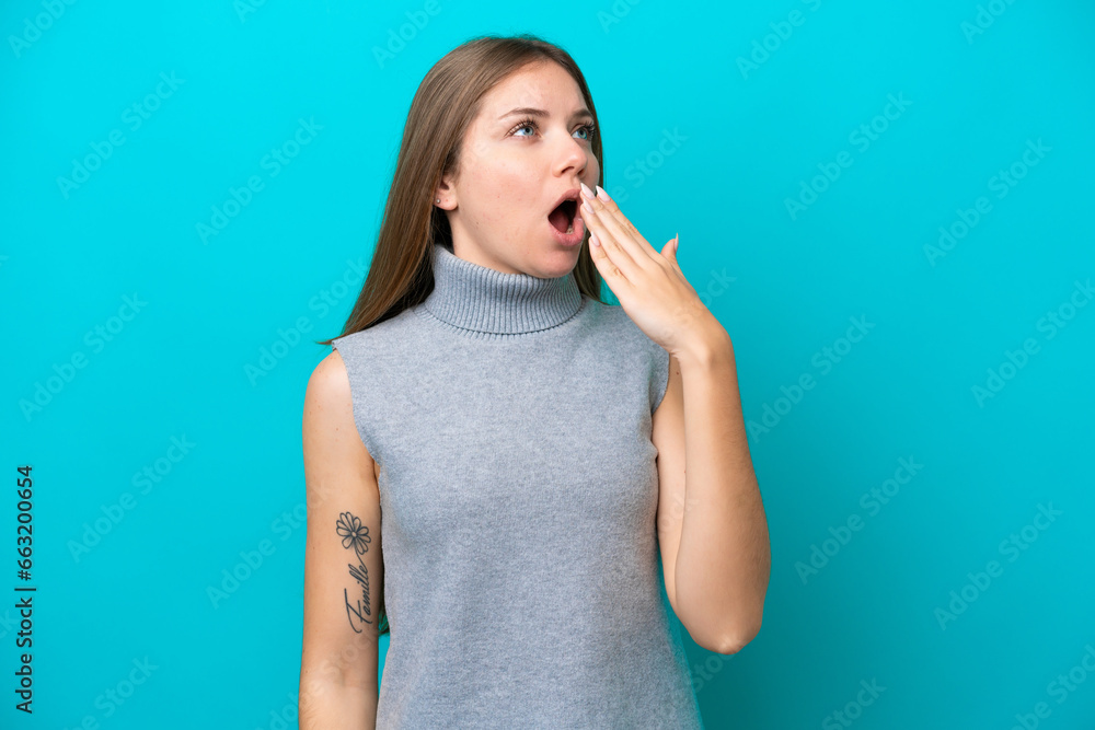Young Lithuanian woman isolated on blue background yawning and covering wide open mouth with hand Young Lithuanian woman isolated on blue background yawning and covering wide open mouth with hand