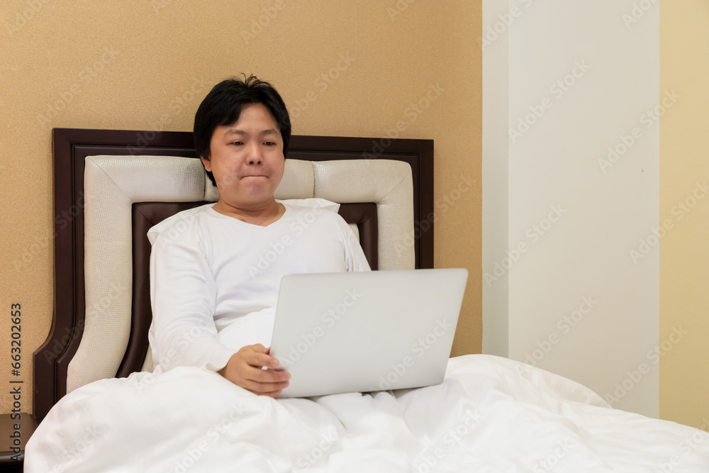 Work from home, a freelancer man leaning against the bed and using his laptop to work online on a bed. Work from home, a freelancer man leaning against the bed and using his laptop to work online on a bed.