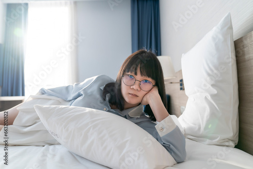 Asian young glasses woman lie on her side on the bed in the morning.