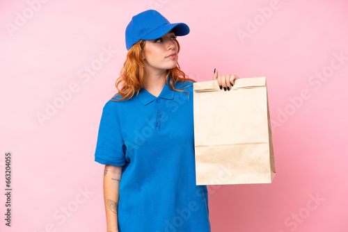 Young caucasian woman taking a bag of takeaway food isolated on pink background looking to the side