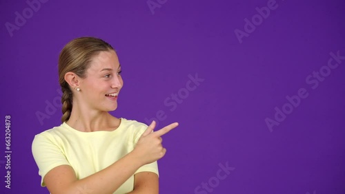Young surprised woman pointing at copy space isolated on purple background.