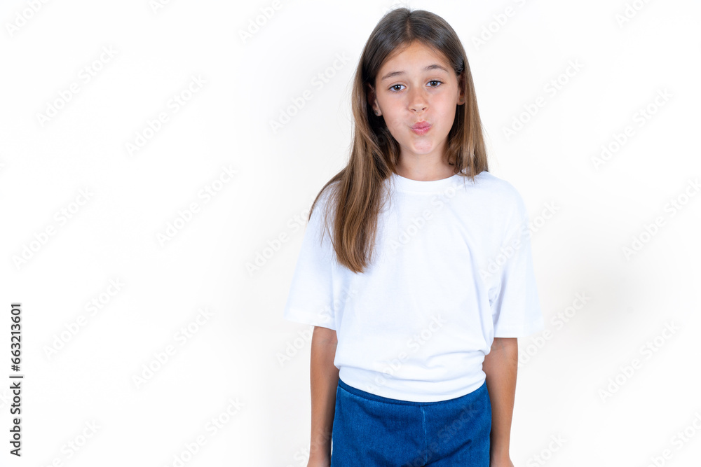 Shot of pleasant looking Beautiful little kid girl wearing white T-shirt , pouts lips, looks at camera, Human facial expressions Shot of pleasant looking Beautiful little kid girl wearing white T-shirt , pouts lips, looks at camera, Human facial expressions
