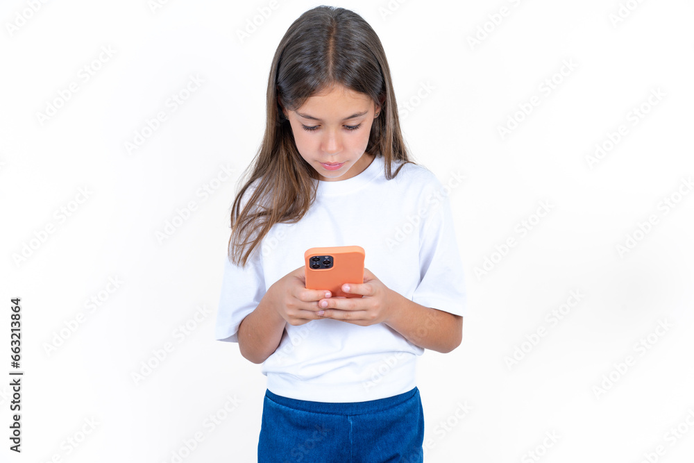 Focused Beautiful kid girl wearing white T-shirt use smartphone reading social media news, or important e-mail Focused Beautiful kid girl wearing white T-shirt use smartphone reading social media news, or important e-mail