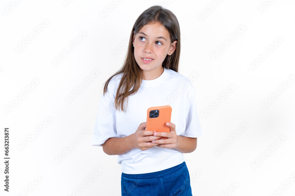 Beautiful kid girl wearing white T-shirt holds telephone hands reads good youth news look empty space advert Beautiful kid girl wearing white T-shirt holds telephone hands reads good youth news look empty space advert
